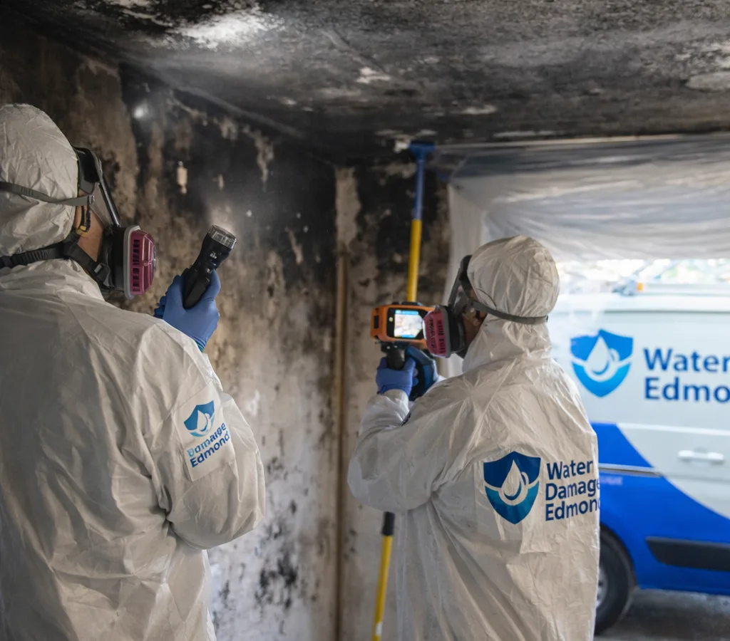 Technicians in protective gear inspecting fire and smoke damage inside an Edmond home with soot staining and containment in place